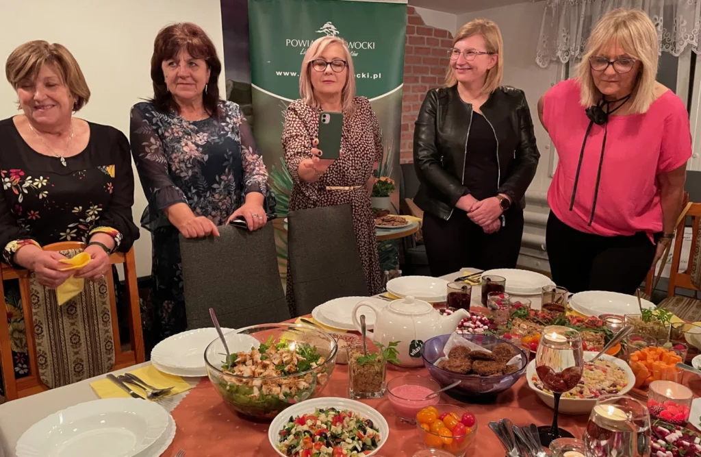 Uczestniczki programu „Żyj Zdrowo” w Otwocku przy stole podczas zakończenia projektu, ze zdrowymi potrawami przygotowanymi przez siebie.